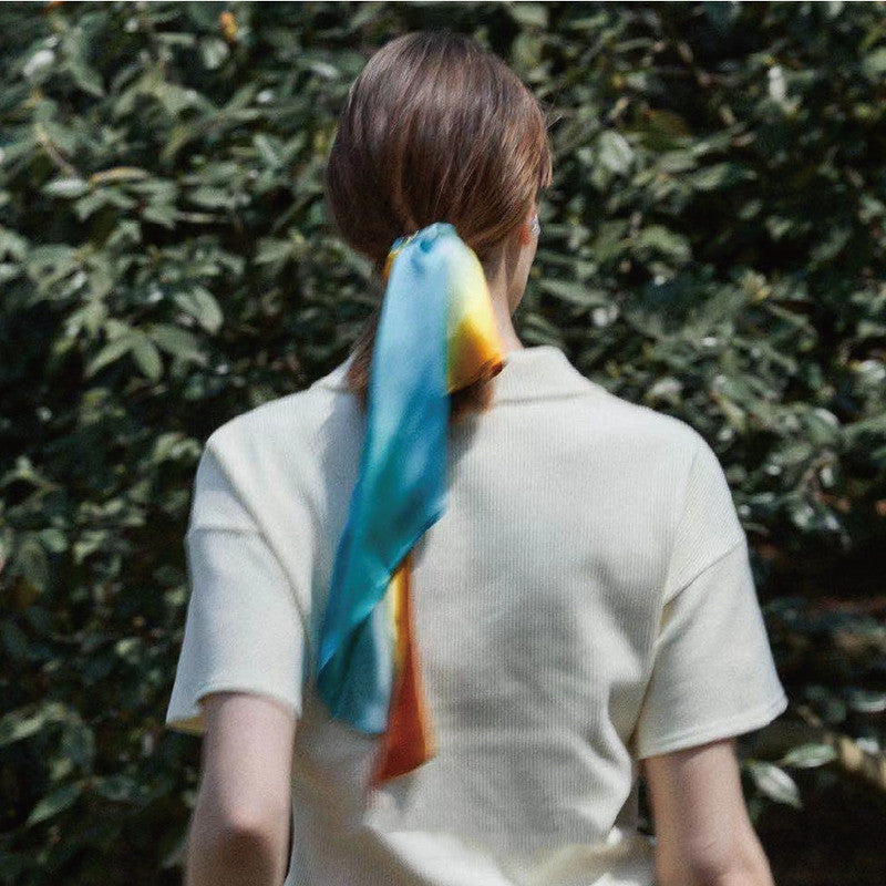 Person wearing a colorful scarf tied around their neck with a green leafy background