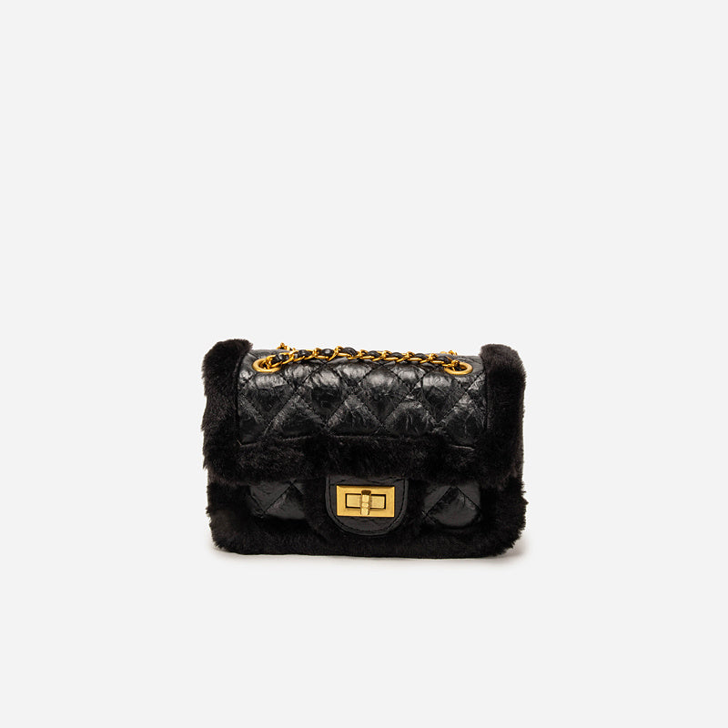 Black quilted handbag with gold accents on a white background