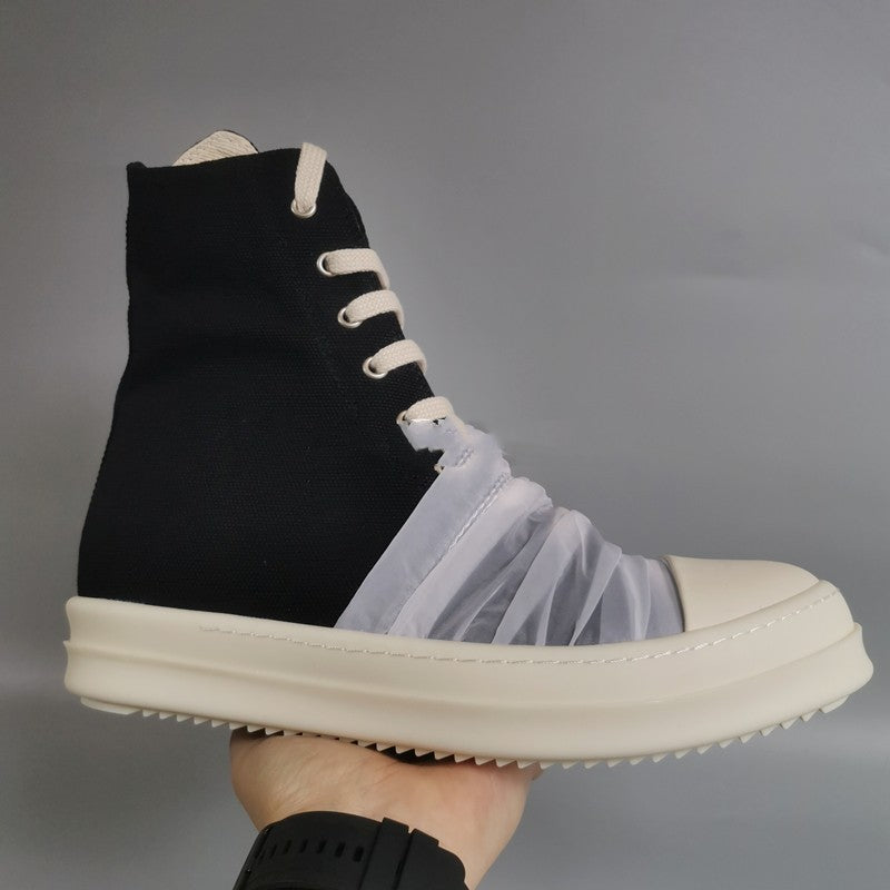 Black high-top sneaker with white laces and sole, worn on a gray background