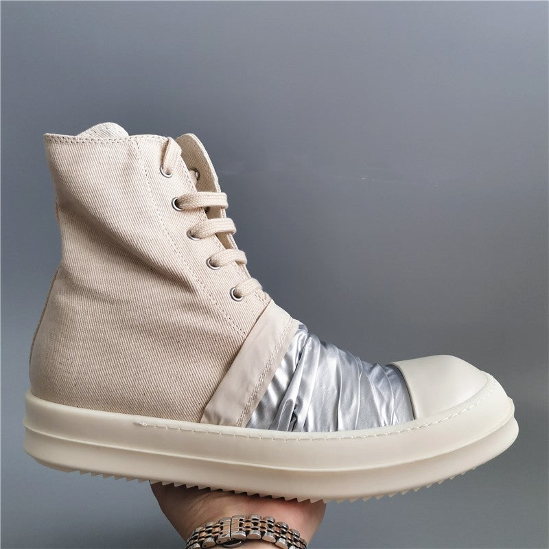 Beige high-top sneaker with metallic sole held by a hand against a gray background