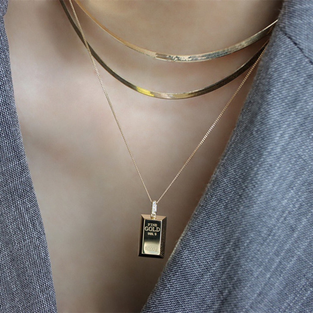 Gold necklace with a gold bar pendant on a mannequin wearing a gray cardigan.
