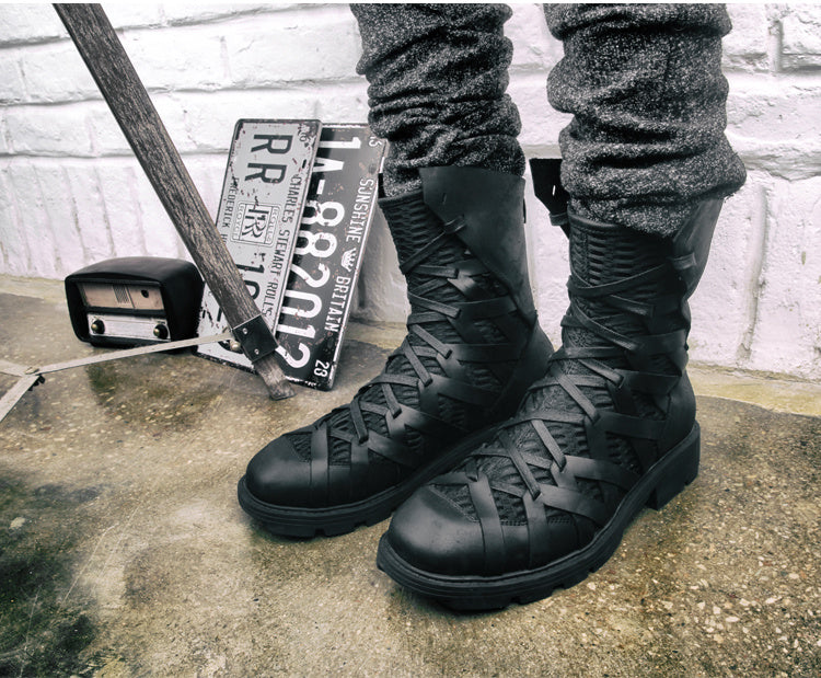 Black combat boots worn by a person standing on a concrete surface with a brick wall in the background.