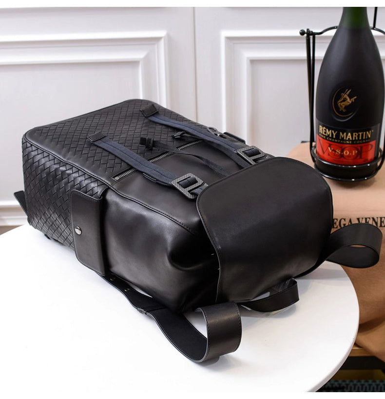 Black woven leather bag on a white surface with a bottle of Remy Martin cognac in the background.
