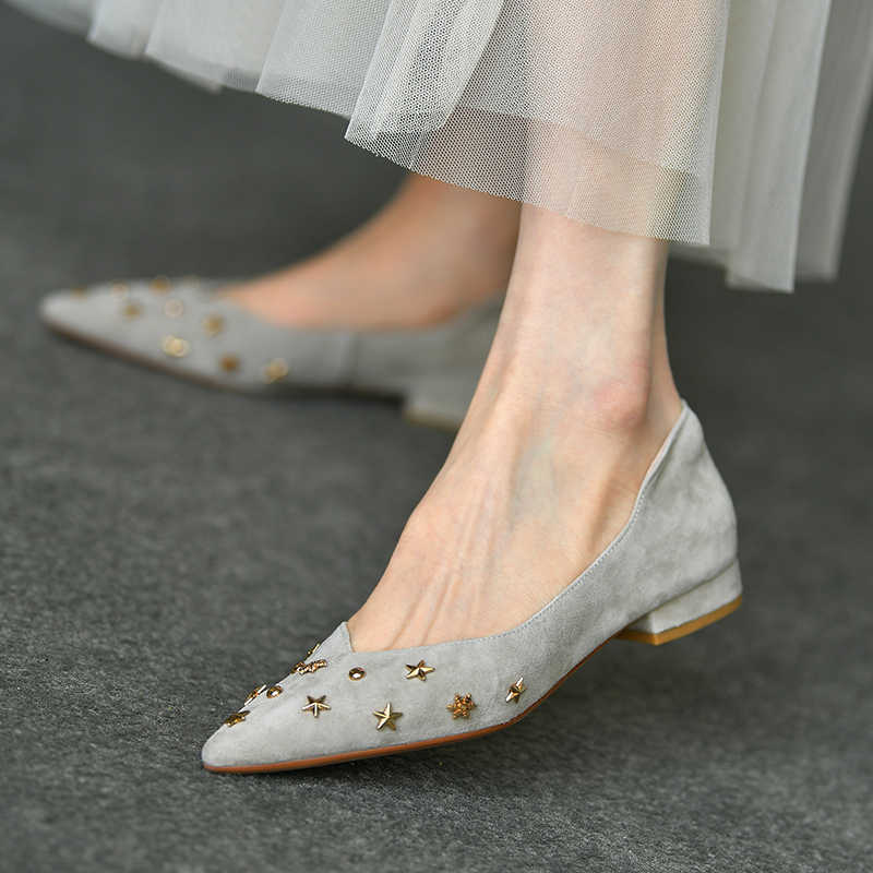 Gray suede shoes with decorative studs worn by a person on a dark surface