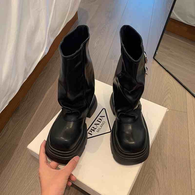 Black boots on a white platform with a Prada logo, on a wooden floor.