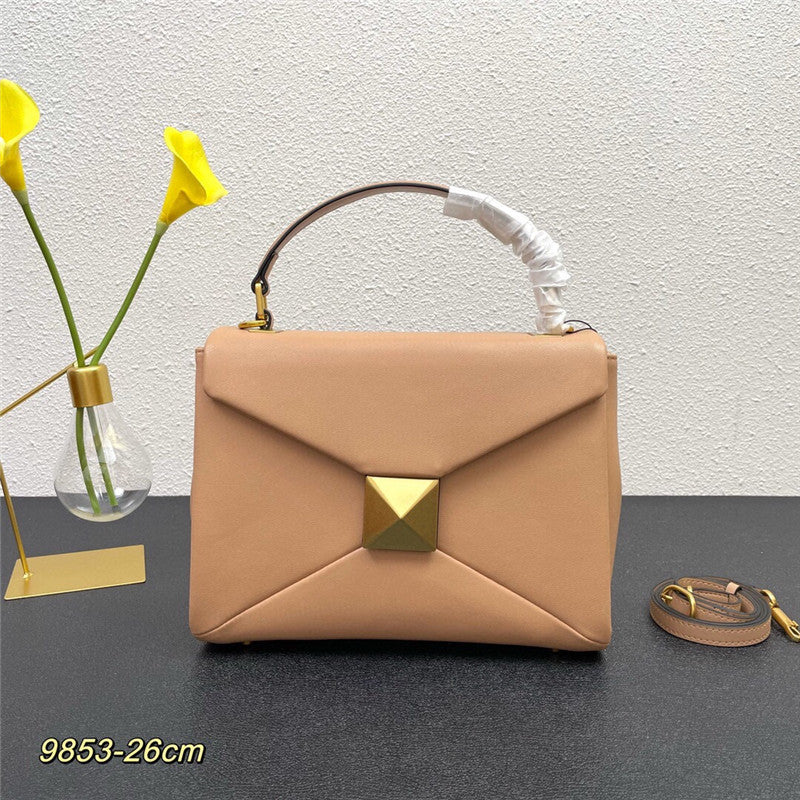 Beige handbag with gold accents on a dark surface with a light gray textured wall background