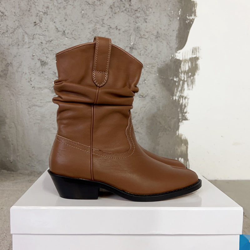 Brown leather boot on a white pedestal against a textured wall.