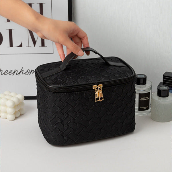 Black woven cosmetic bag with gold clasp held by a hand on a white surface.