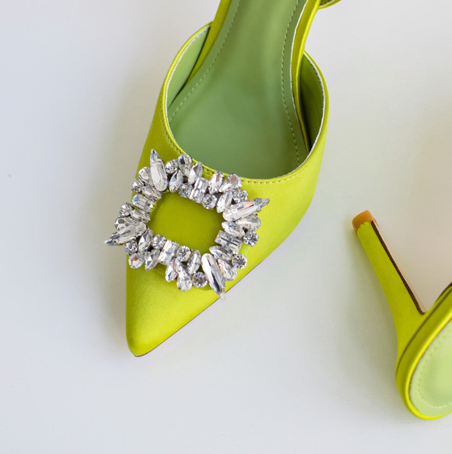Green high-heeled shoes with crystal embellishments on a light background