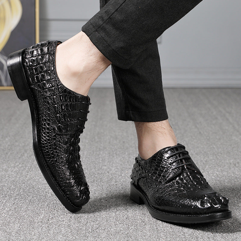 Black crocodile-patterned shoes worn with black pants on a gray floor.