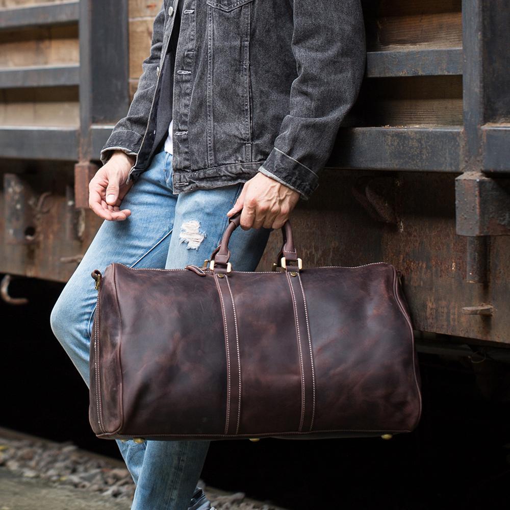 Person holding a brown leather duffel bag against a rustic metal background