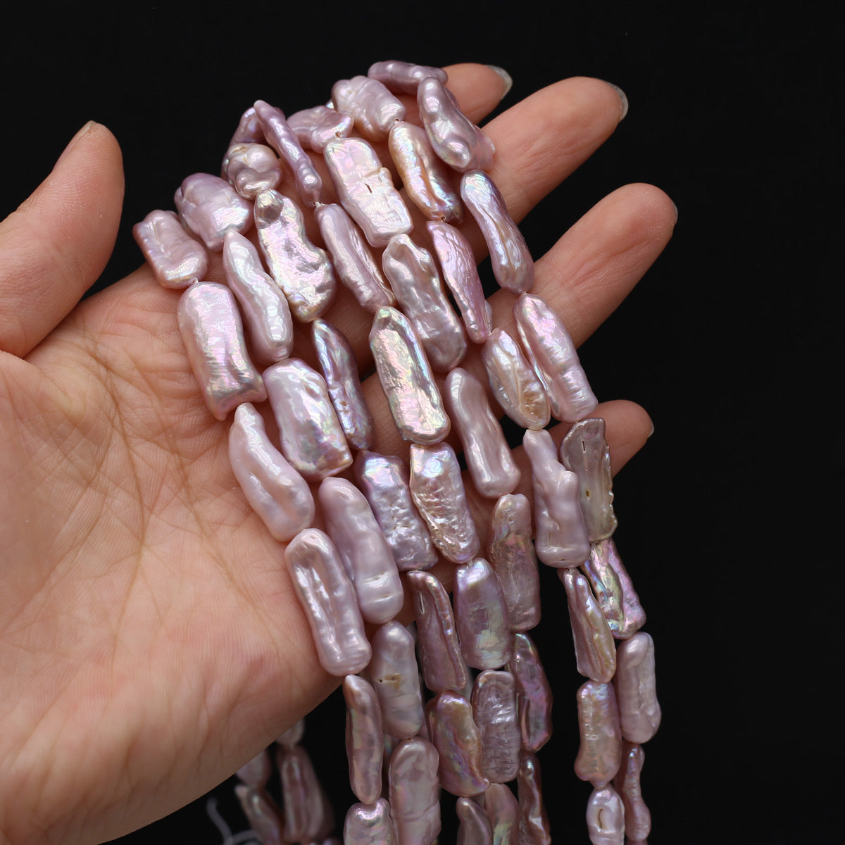 Hand holding a strand of pink pearls against a black background
