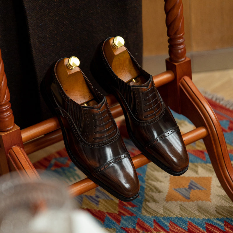 Pair of brown leather shoes on a wooden chair with a patterned rug underneath.