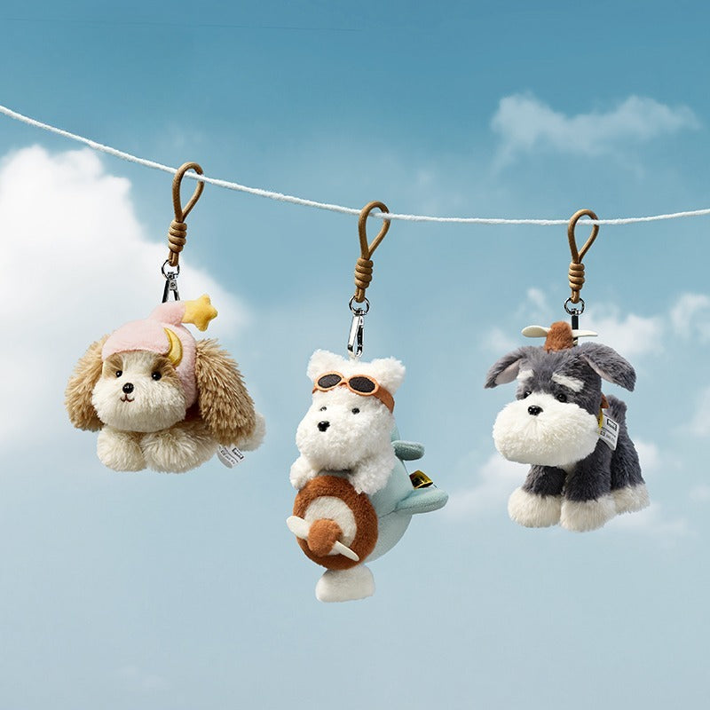 Three plush dog keychains hanging on a string against a blue sky with clouds.