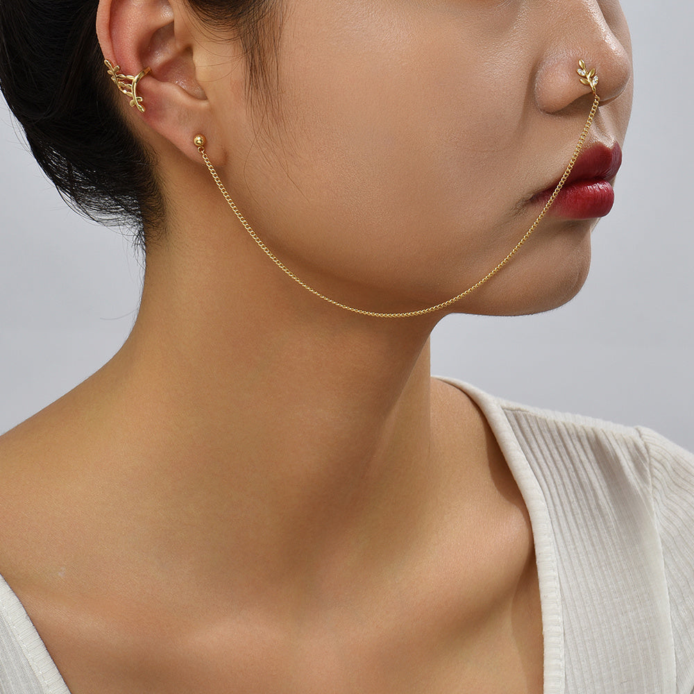 Close-up of a person wearing gold jewelry including earrings and a necklace on a neutral background