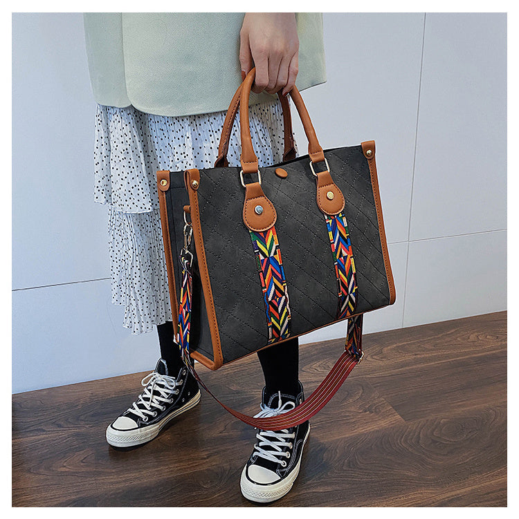 Person holding a black handbag with a colorful strap on a wooden floor.