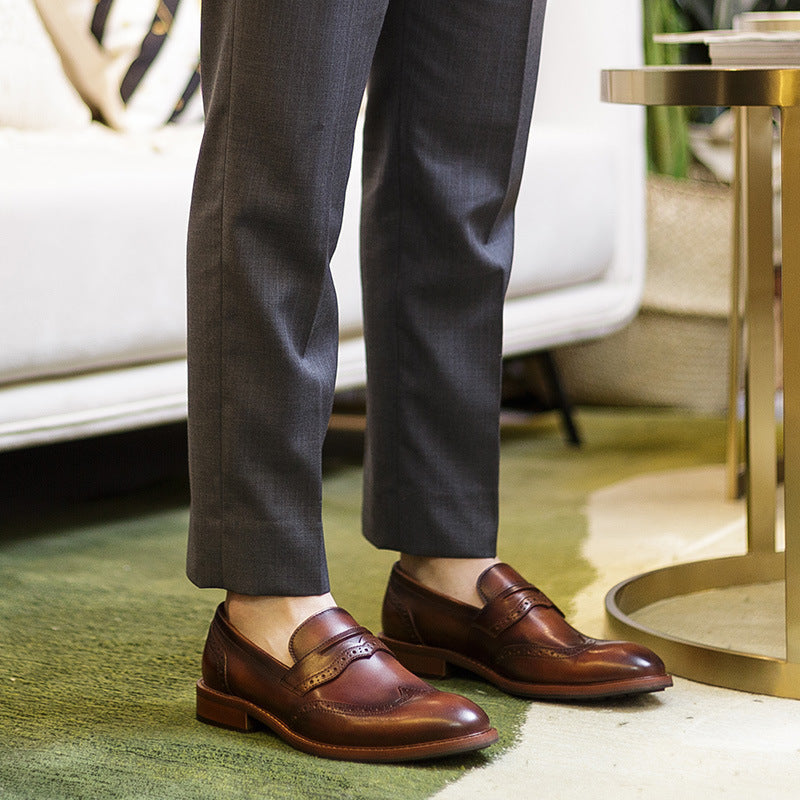 Brown leather shoes worn with gray pants on a carpeted floor.