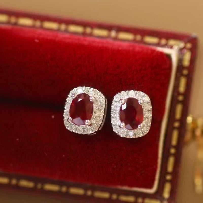 Pair of earrings with red gemstones and diamond-like stones on a red cushioned jewelry box.