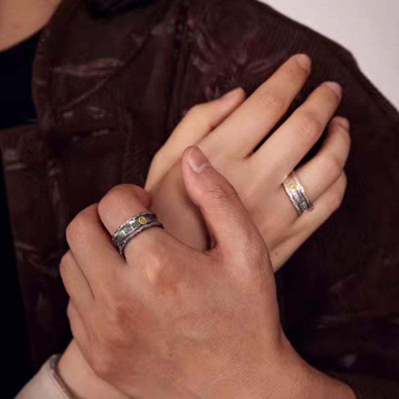 Close-up of two hands with silver rings on a dark background