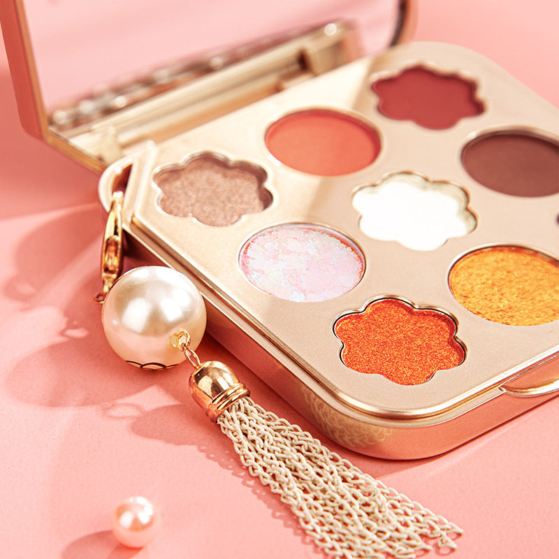 Makeup palette with colorful shades and a decorative earring on a pink background