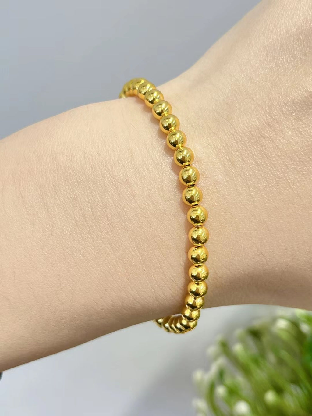Gold beaded bracelet on a wrist with a neutral background