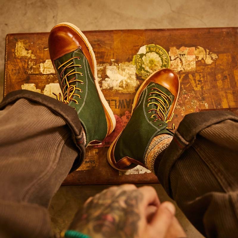 Green and brown leather shoes on a vintage suitcase with a tattooed hand.