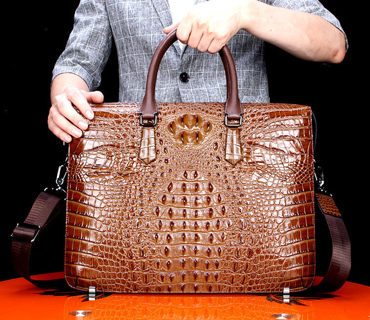 Brown crocodile skin briefcase held by a person against a black background