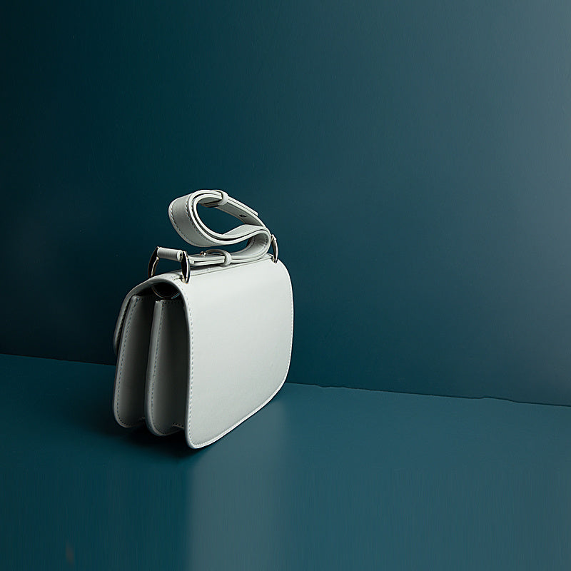 White handbag with a unique handle design on a dark teal background