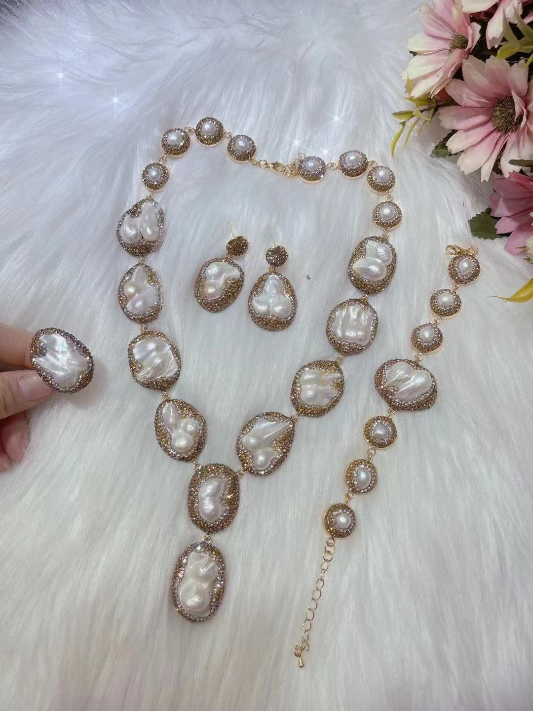 Pearl necklace and earrings set on a white fur background with flowers.