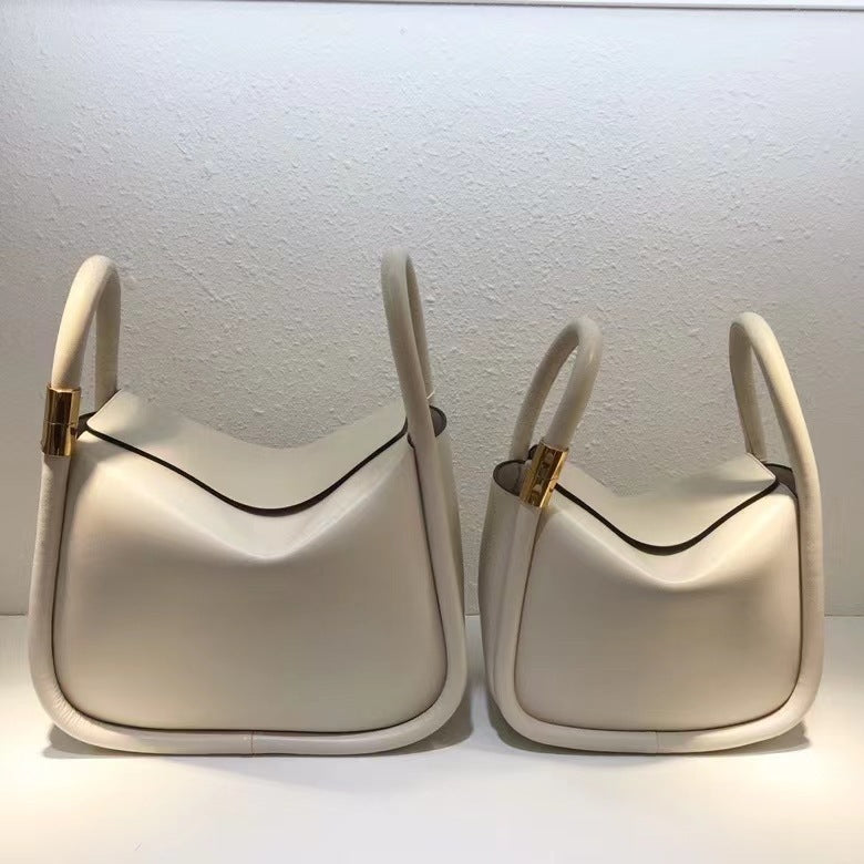 Two cream-colored handbags with gold accents on a white background