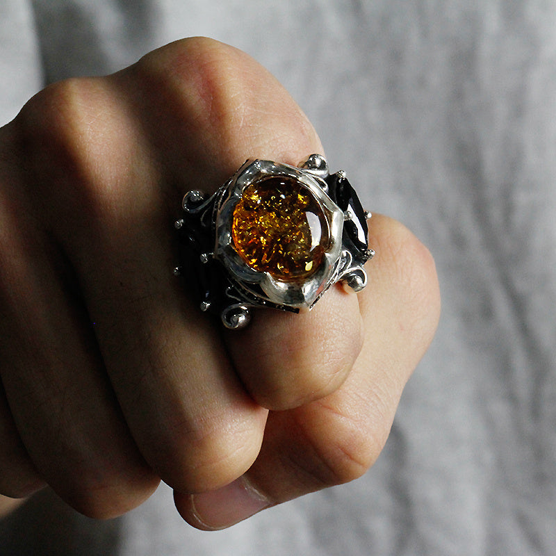Close-up of a hand wearing a silver ring with a large amber stone against a neutral background