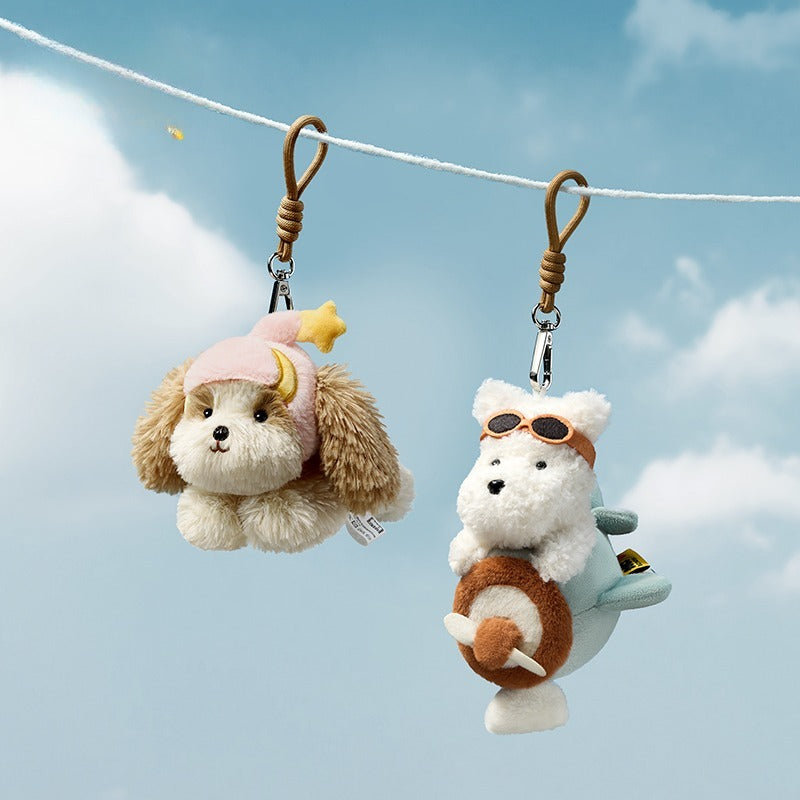 Two plush dog keychains hanging on a string against a blue sky with clouds.