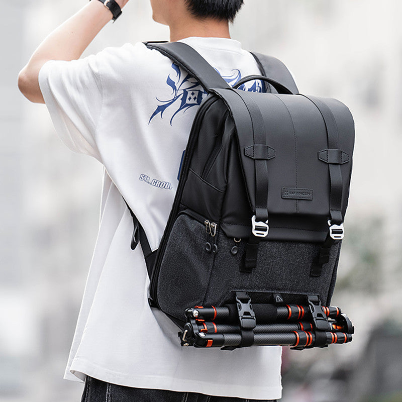 Person wearing a black backpack with a camera tripod attached, blurred background