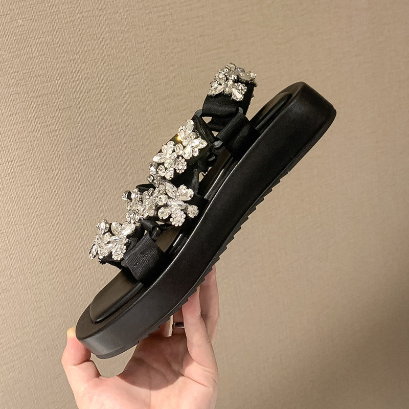 Black sandal with floral embellishments held against a beige background