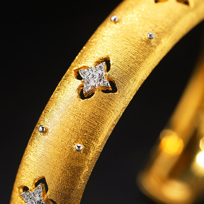 Gold bracelet with star-shaped diamond embellishments on a black background