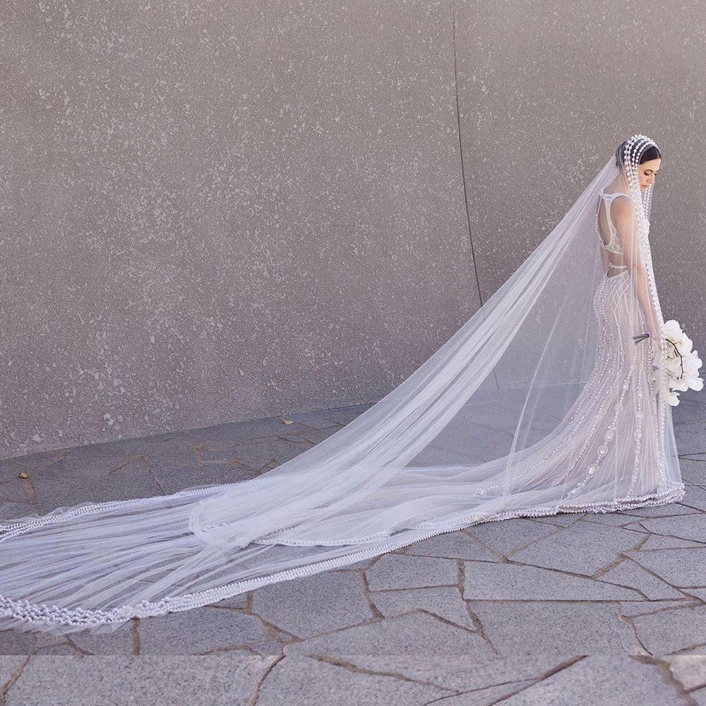 Woman in a wedding dress with a long veil against a gray wall.