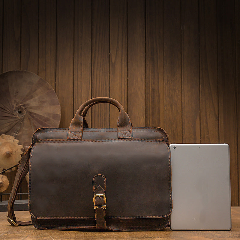 Brown leather briefcase next to a tablet on a wooden surface with a wooden panel background