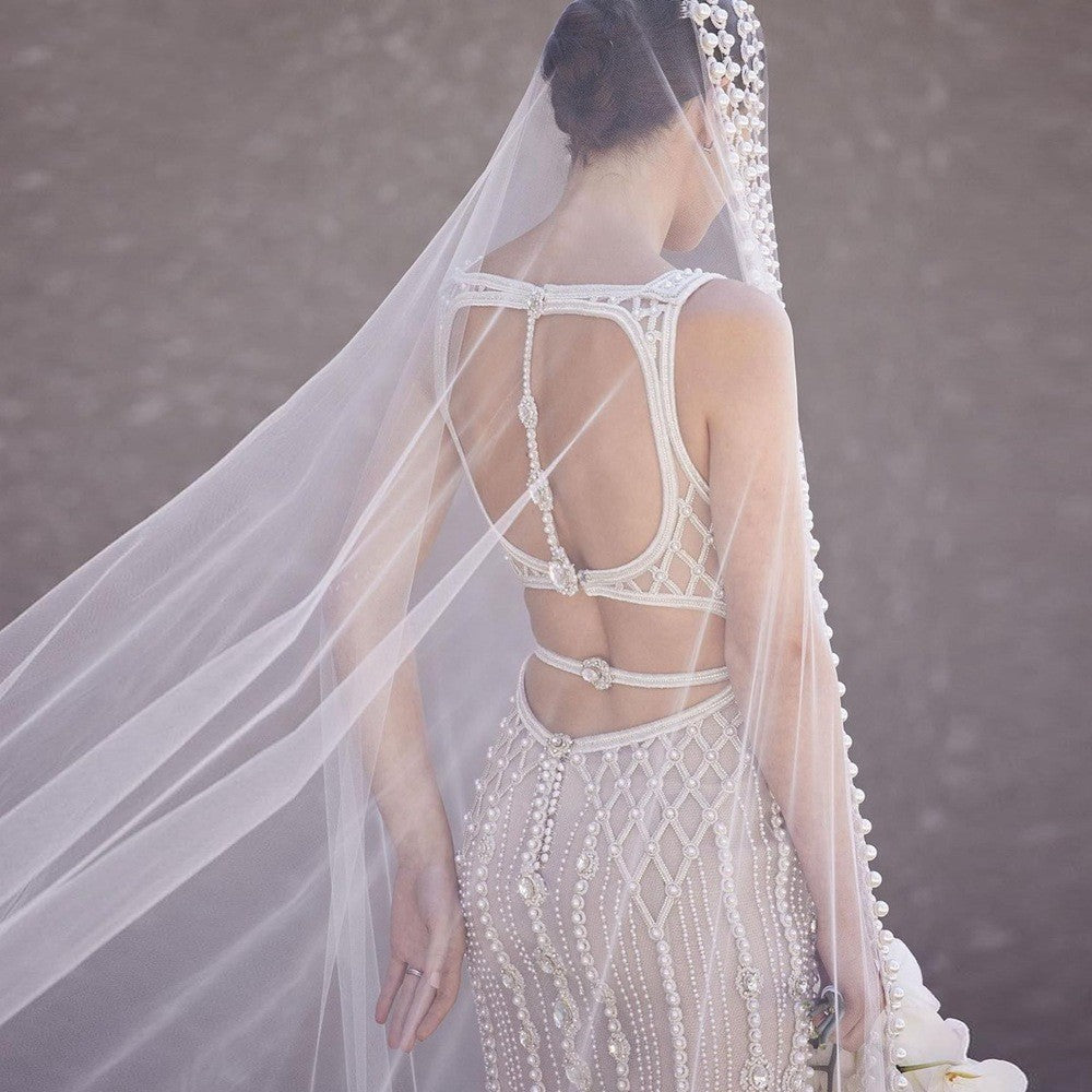 Woman wearing a white wedding dress with intricate detailing and a long veil.