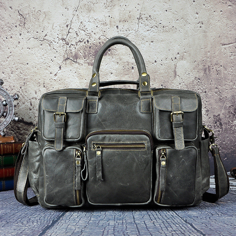 Gray leather bag with multiple pockets and straps on a textured surface