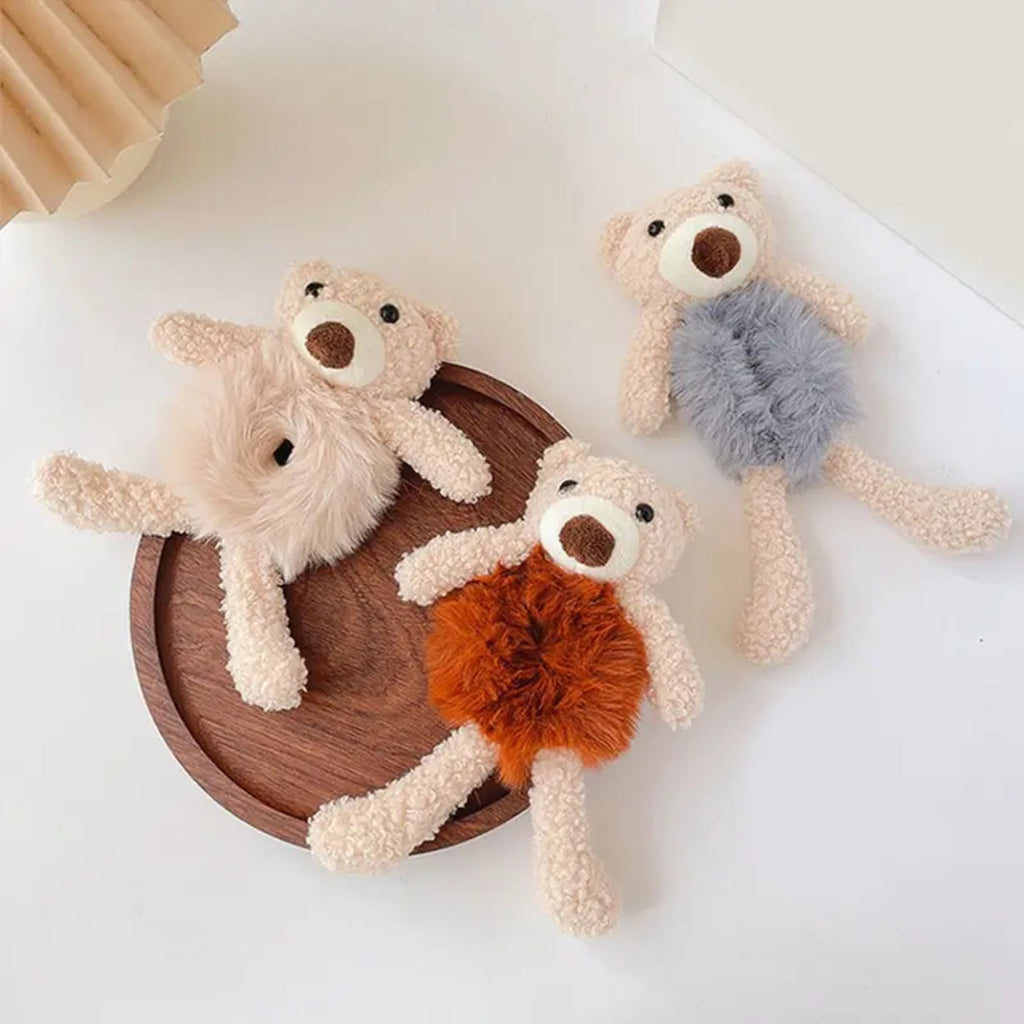 Three plush toys resembling bears with different colored fur on a wooden plate.
