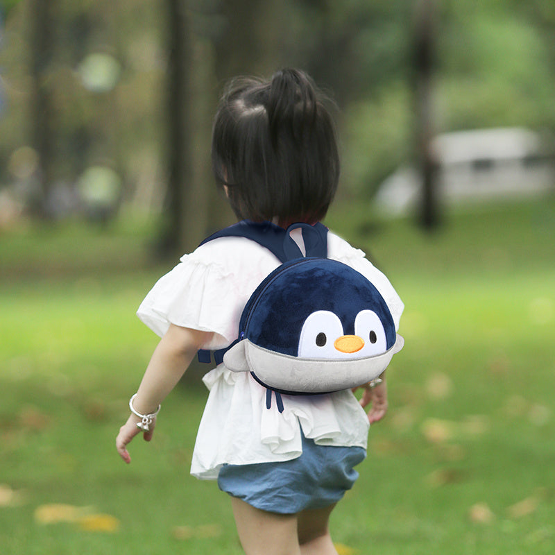 Child wearing a penguin backpack in a park