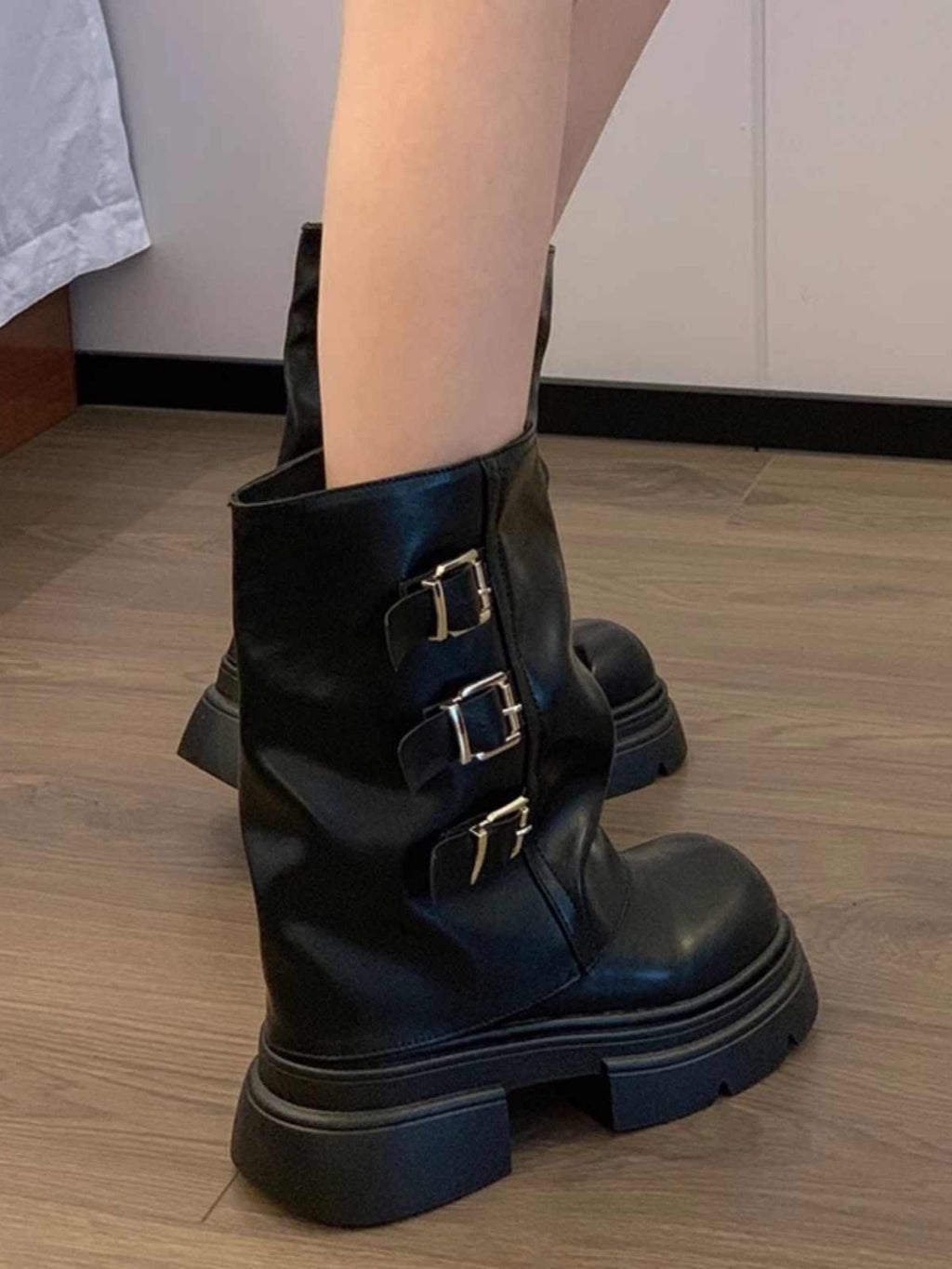 Black leather boots with buckles worn by a person on a wooden floor.