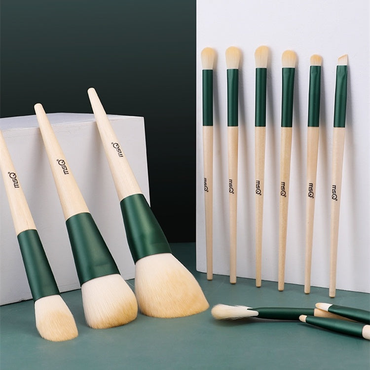 Set of makeup brushes with green and beige handles on a green surface.