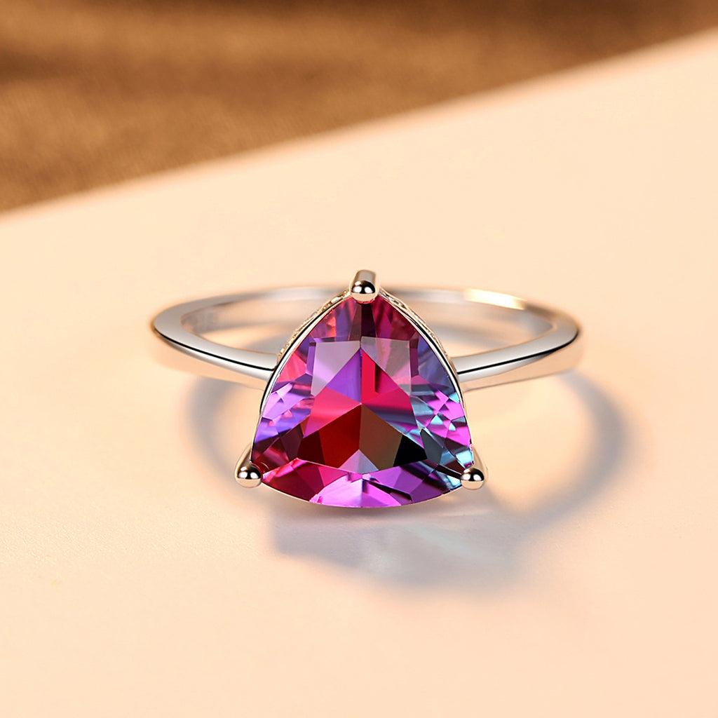 Ring with a teardrop-shaped multicolored gemstone on a beige background