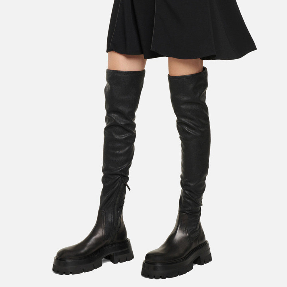Black leather knee-high boots worn with a black skirt on a white background
