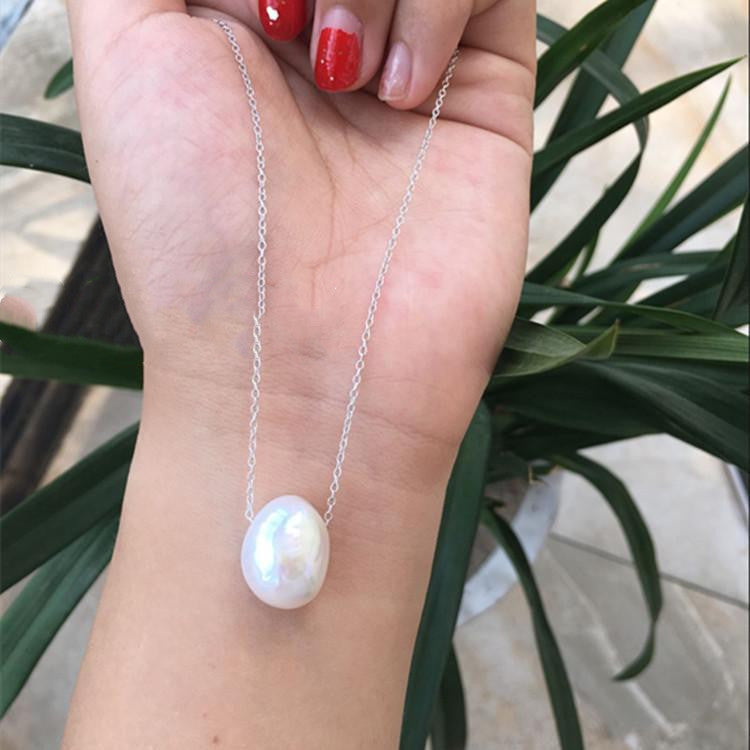 Pearl necklace on a hand with red nail polish, against a blurred green plant background