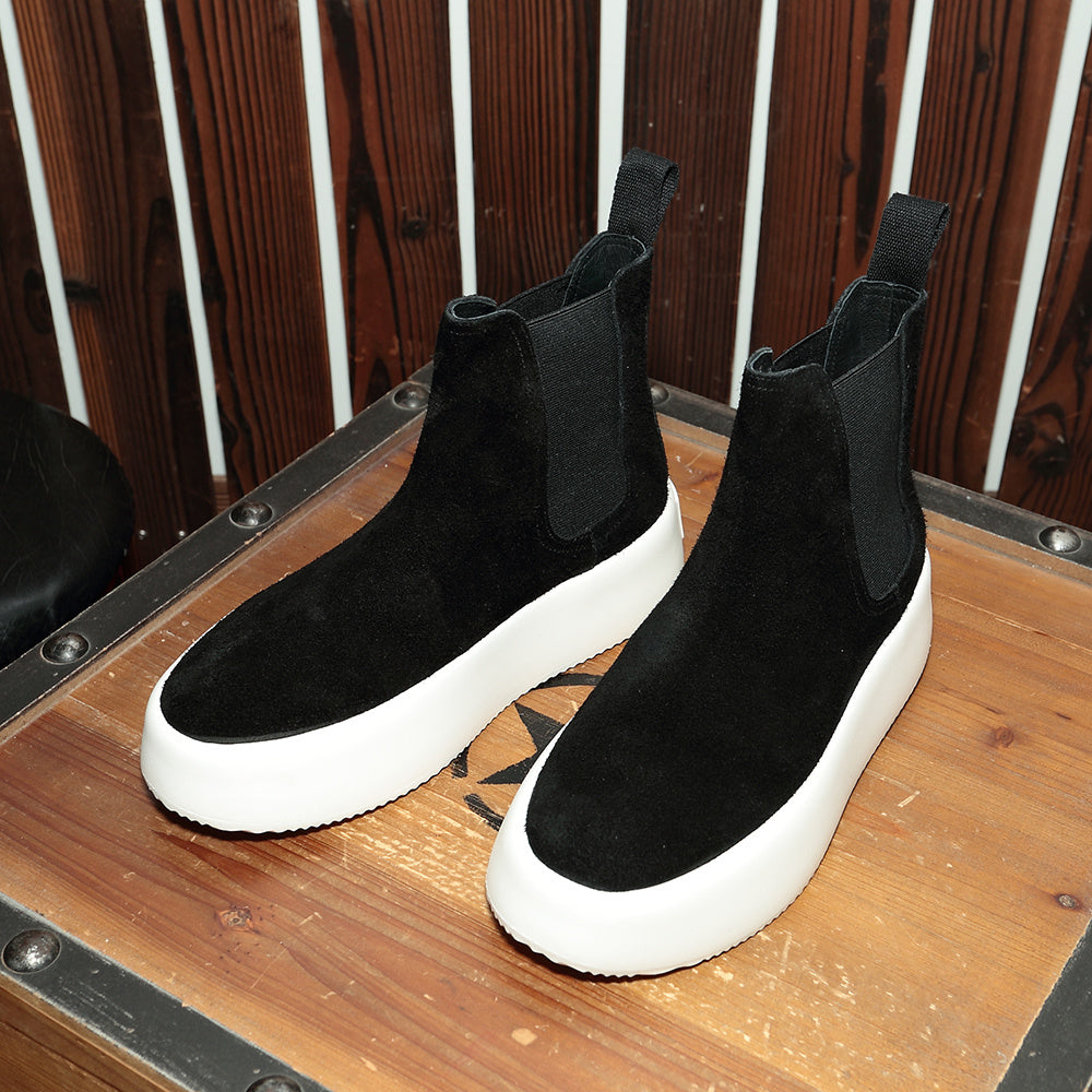 Black ankle boots with white soles on a wooden surface