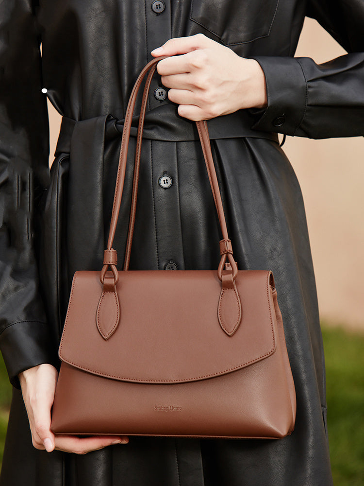 Brown leather handbag held by a person wearing a black coat.