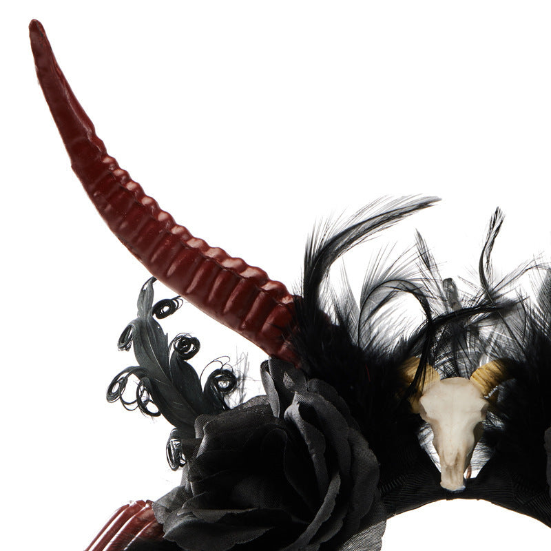 Decorative headpiece with red horns, black feathers, and a small skull on a white background