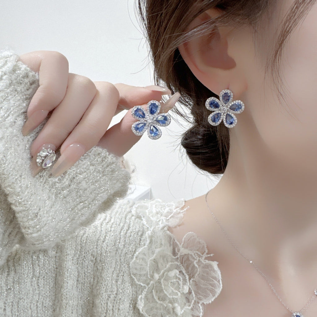 Close-up of a person wearing blue flower-shaped earrings with a blurred background